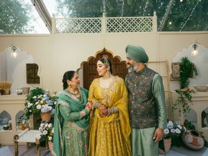 Wedding attire in green and yellow tones displayed against white interior decor with floral arrangements.