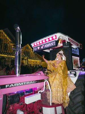 Person in flowing gold dress poses dramatically on pink Farmtrac tractor at night.