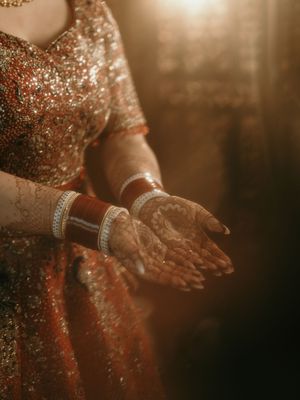 Detailed shot of hands decorated with henna and bangles against a sparkly dress background.