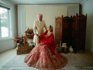 Elegant wedding decor featuring a red lehenga and traditional carved wooden screens in a bright interior setting.
