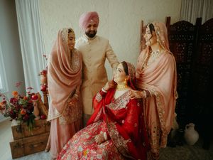 Wedding party poses in coordinated pink and beige outfits with ornate red bridal lehenga.