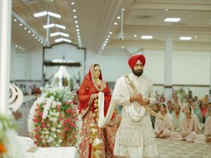 Traditional Sikh wedding ceremony taking place in a brightly lit indoor venue with decorative floral arrangements.