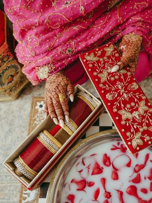Close-up of intricate henna designs on hands holding traditional Indian wedding items against pink fabric.