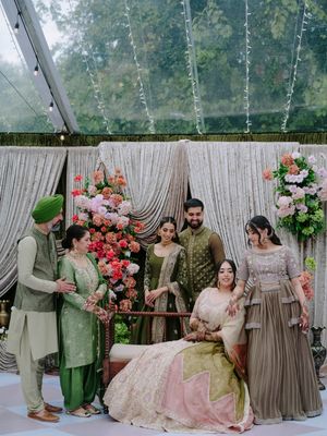 Wedding party in coordinated outfits of sage green and pink posing with floral decorations.