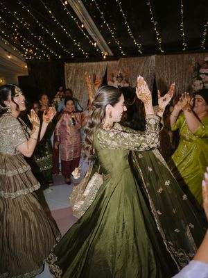 People dancing in historical period costumes including green and brown ball gowns under twinkling string lights.