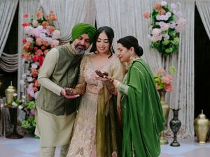 Wedding celebration with guests in green and beige traditional outfits with floral backdrop.