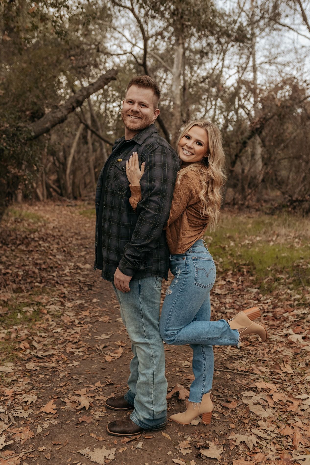 A couple in casual attire shares playful moments among fallen autumn leaves in a wooded setting in San Diego.