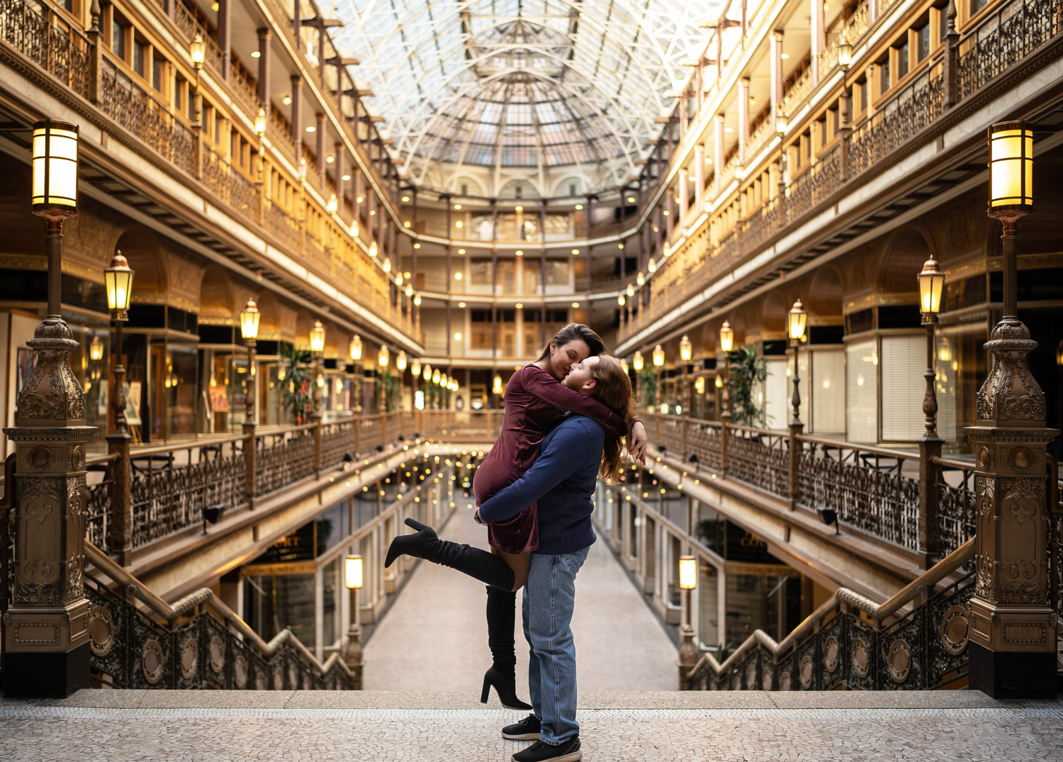 A couple embraces in a romantic pose inside Cleveland Arcade's historic Victorian-era shopping mall with ornate architecture.