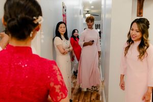 Women in pink and red dresses prepare for a wedding ceremony in a decorated hallway.