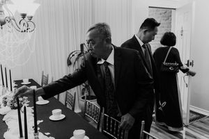 Black and white photo of elegantly dressed guests arranging place settings at wedding reception table.