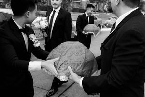 Groomsmen in black suits hold ornate trays with wedding gifts outside.