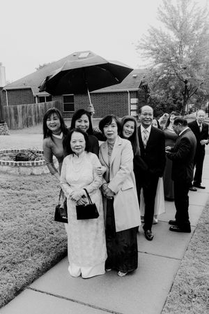 Family group poses under umbrella on sidewalk during rainy outdoor wedding event.
