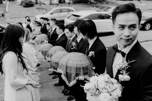 Groom with bouquet leads groomsmen carrying traditional Vietnamese lacquered wedding trays.
