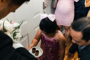 Young girl in purple dress offers tea cups at traditional Vietnamese wedding ceremony.