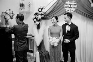 Bride and groom smiling with guests at a Chinese wedding ceremony with double happiness symbol decor.
