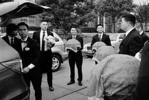 Groomsmen in suits carry ceremonial trays outside during a Vietnamese wedding procession.