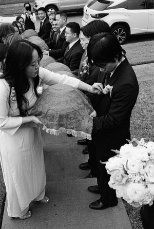 Woman in white ao dai hands ceremonial tray to groom during Vietnamese wedding.