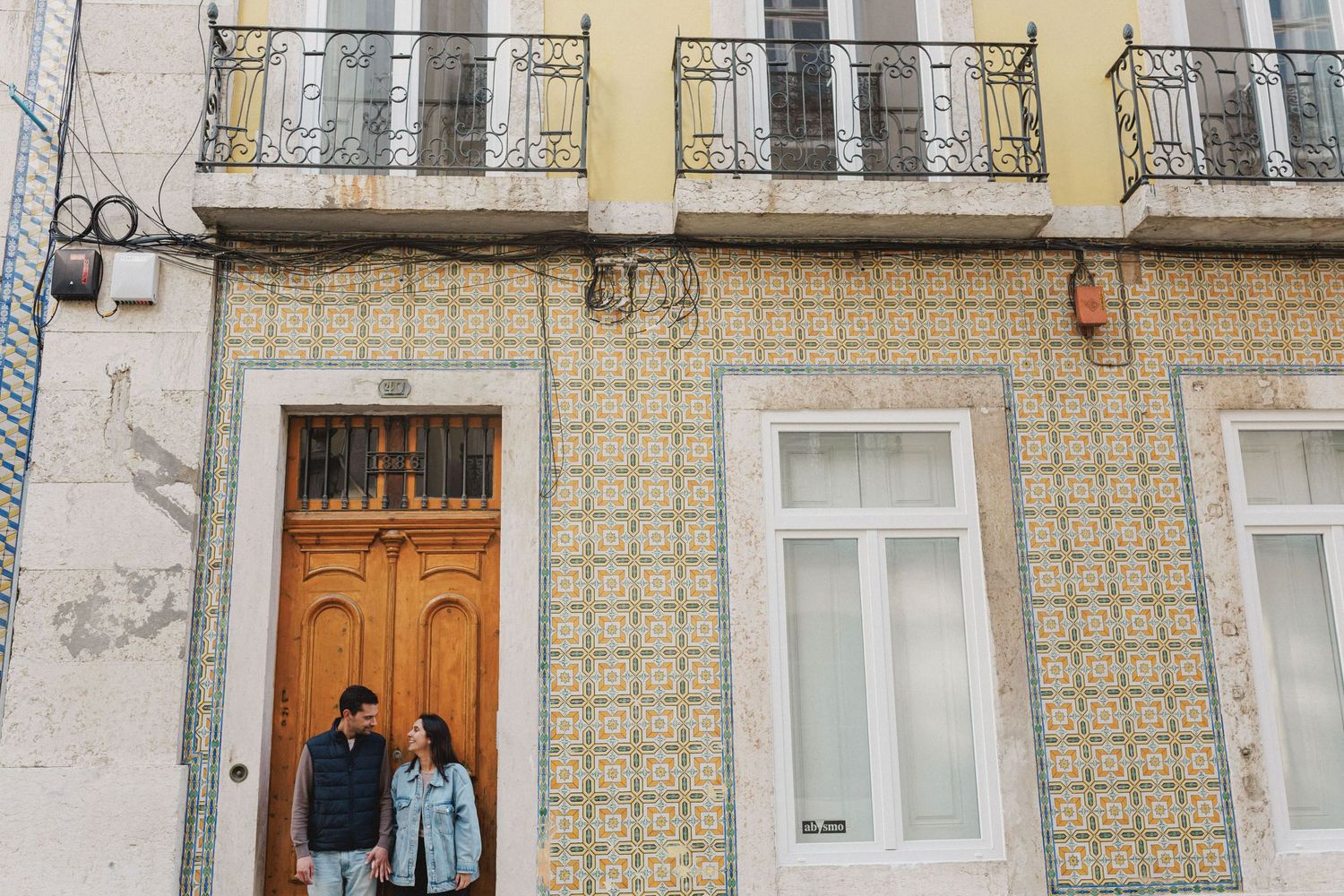 Smiling couple holding hands in front of traditional Lisbon doorway with azulejo tiles, Baixa pre wedding session
