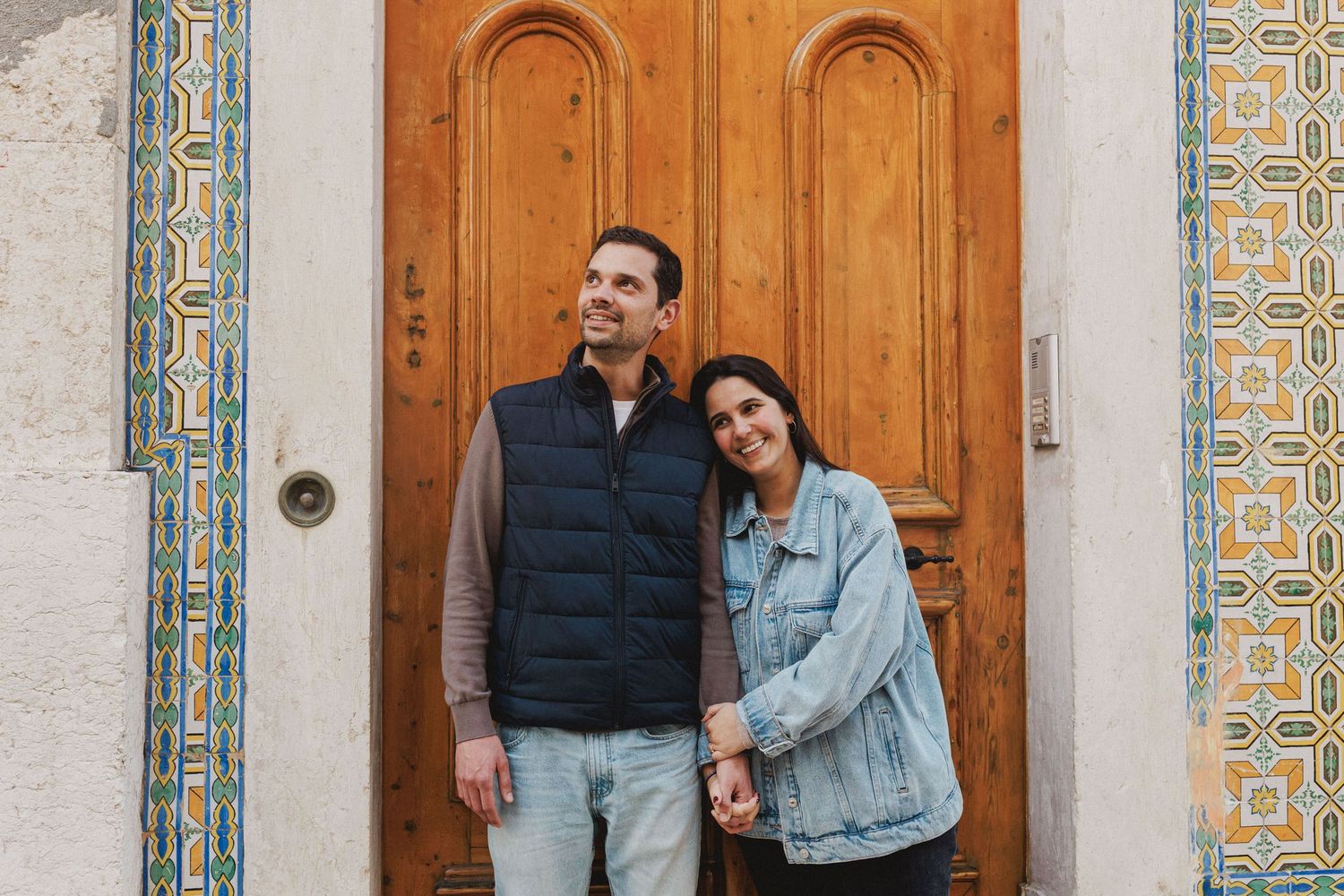 Couple standing by colorful azulejo facade and wooden door in Baixa Lisbon during pre wedding photoshoot