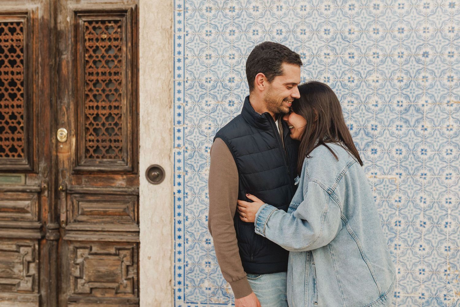 Couple walking past traditional Lisbon building with blue tiles and wooden door during pre wedding session