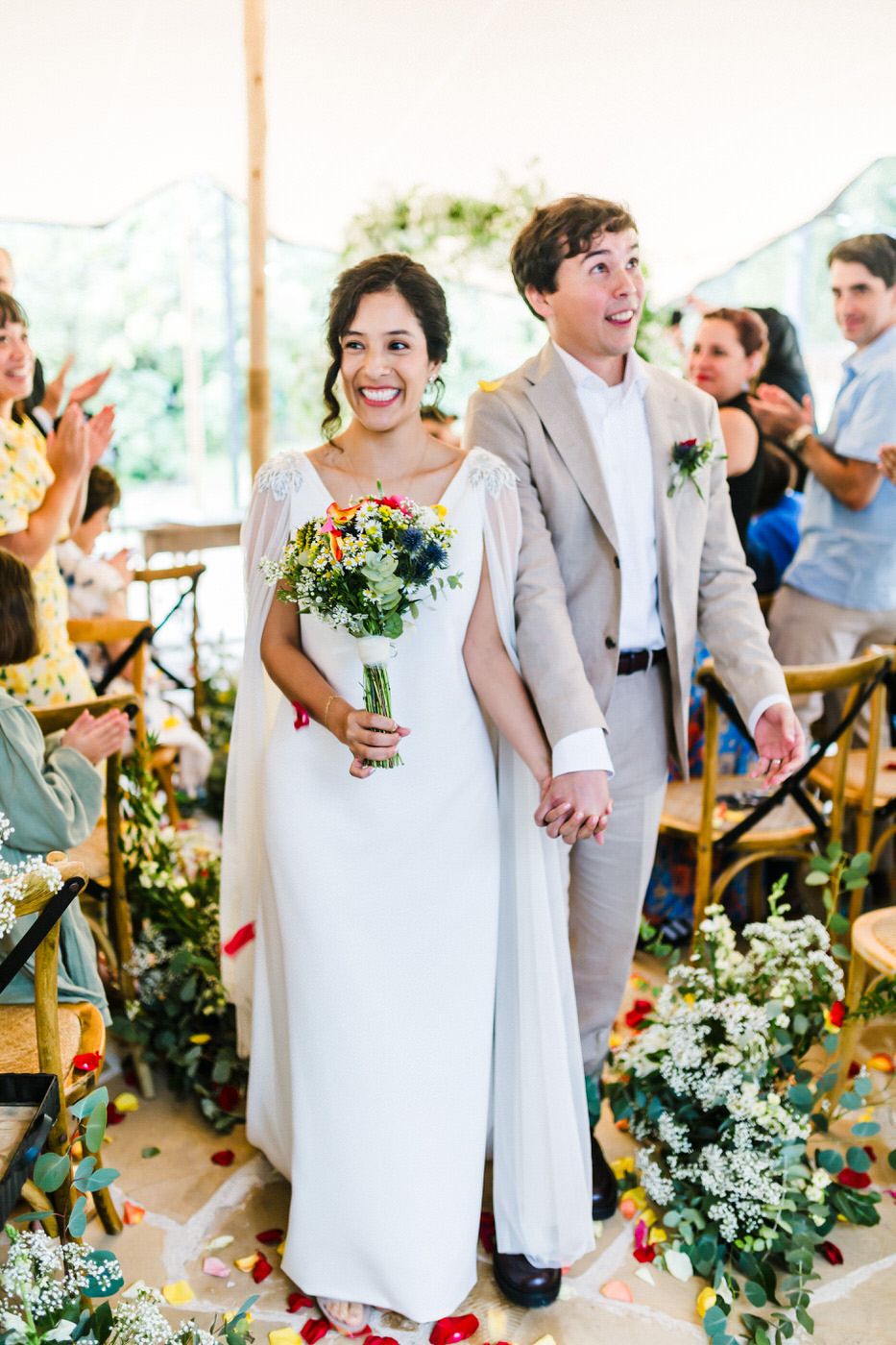 A couple celebrates during their outdoor wedding ceremony surrounded by floral arrangements and guests.