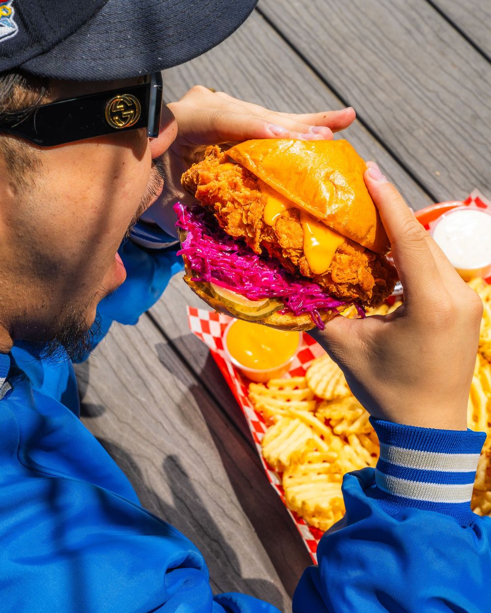 A sequence of photos showing someone taking bites of a bright orange burger with vibrant purple slaw on a wooden deck.