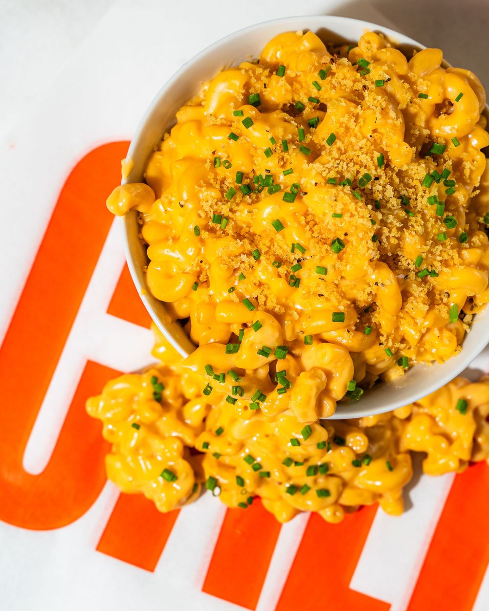 A close-up view of creamy macaroni and cheese topped with fresh herbs and breadcrumbs in a white bowl.