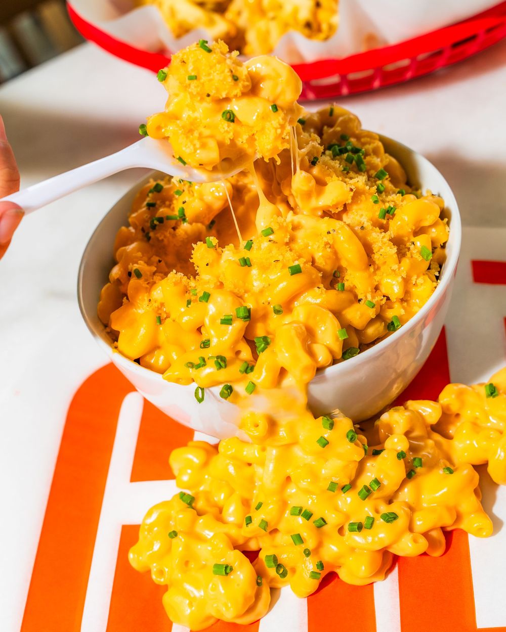 Creamy mac and cheese topped with fresh chives served in a white bowl on a red and white striped surface.