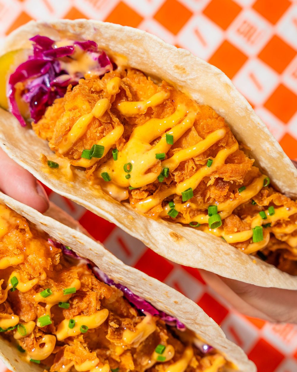 Homemade shawarma pitas topped with red cabbage and fresh herbs arranged in a row on orange checkered paper.
