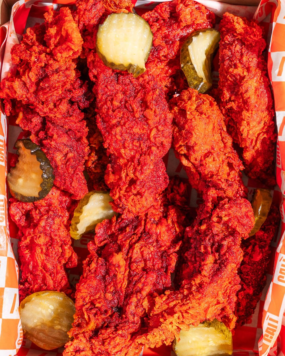 Bright red tandoori chicken pieces garnished with cucumber slices arranged in rows on a serving platter.