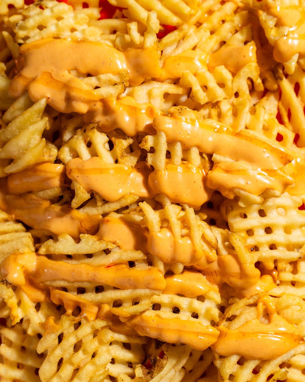 Close up of waffle fries covered in melted cheese sauce showing crispy ridged texture and golden orange color.