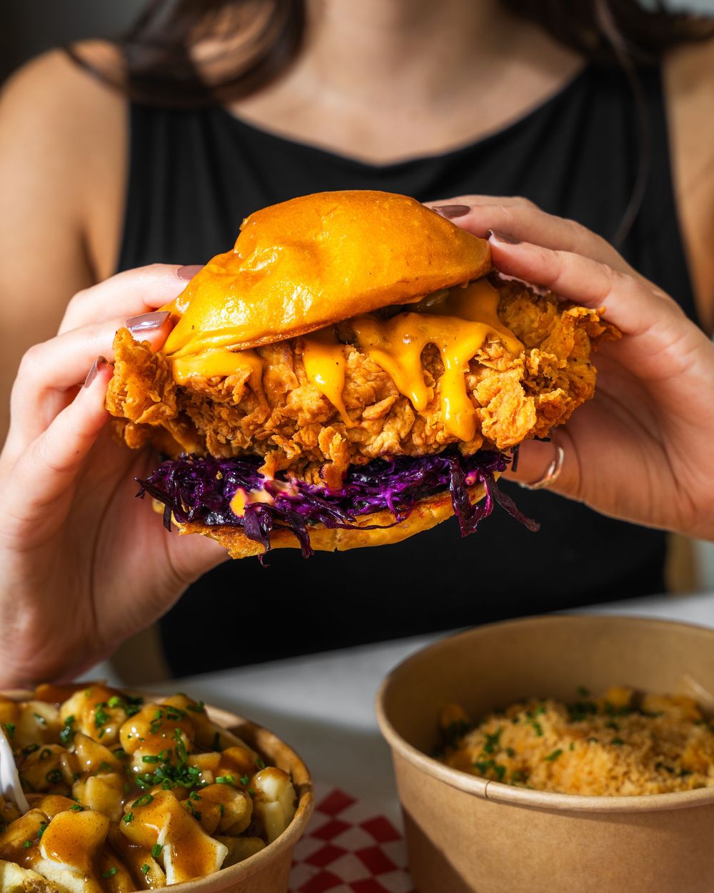 Hands pull apart a sandwich filled with purple cabbage slaw and golden fried chicken on a dark background.