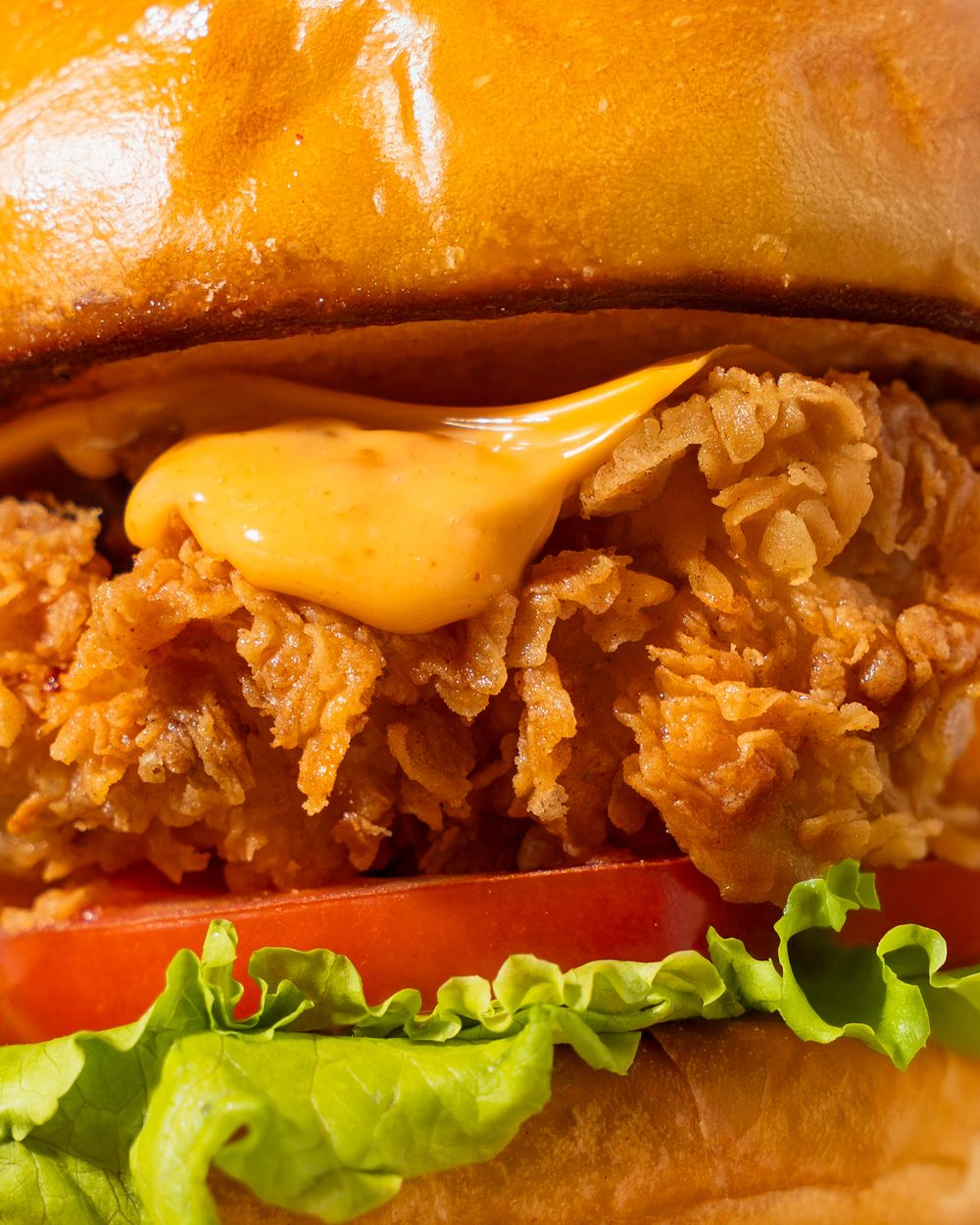 Close-up of a crispy chicken sandwich with melted cheese, lettuce and tomato on a toasted bun.