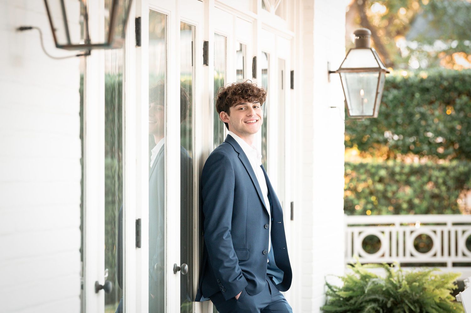 A person in a navy suit stands on an elegant white porch with classic columns and architectural details.
