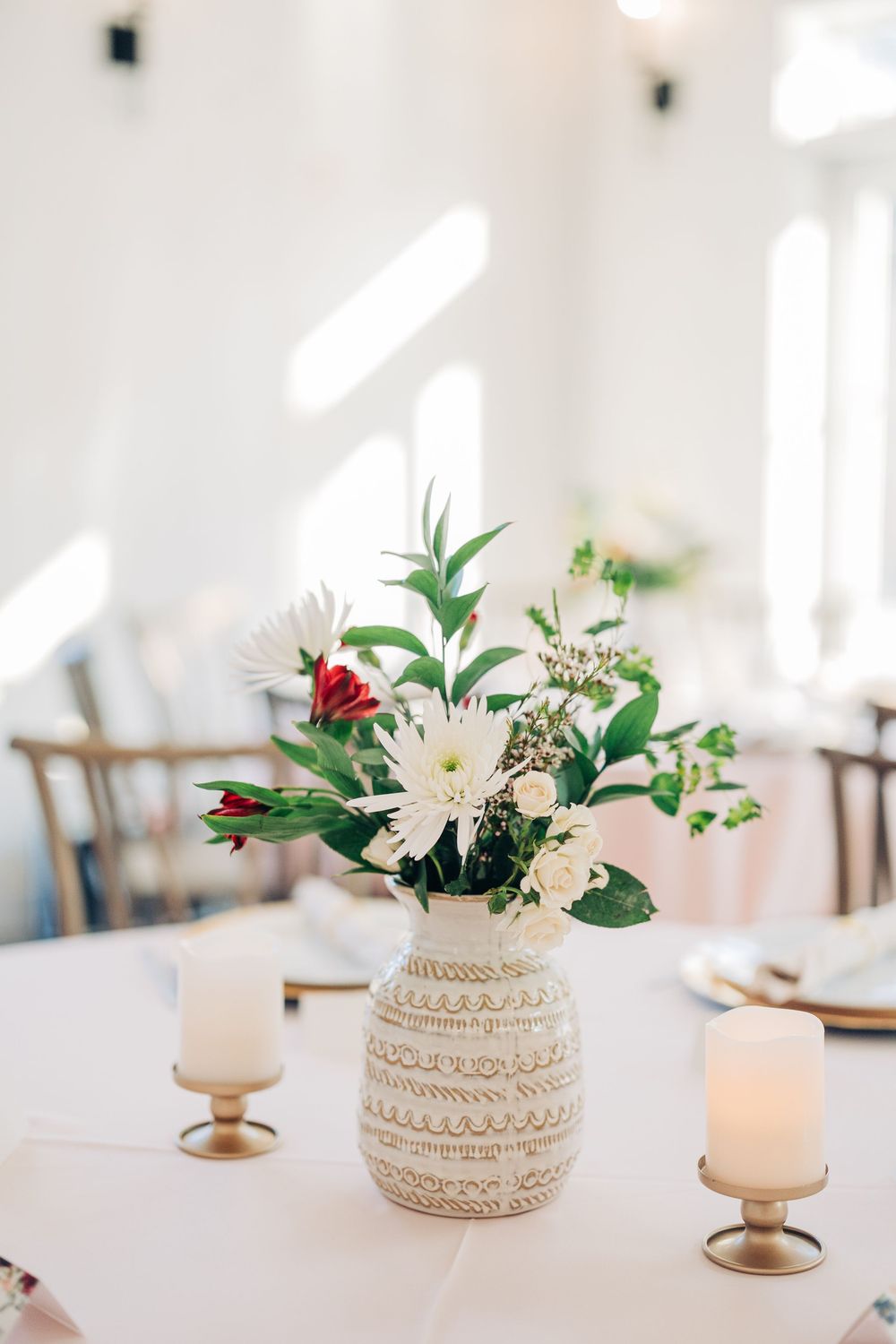 Elegant table settings with white floral centerpieces in woven baskets and gold candleholders on a light surface.