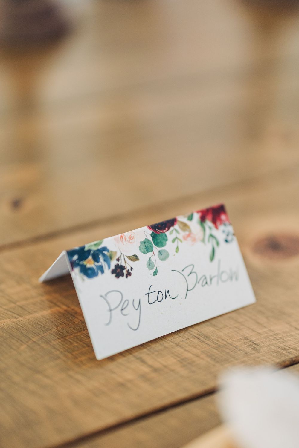 Delicate floral place cards with handwritten names displayed on a rustic wooden table.