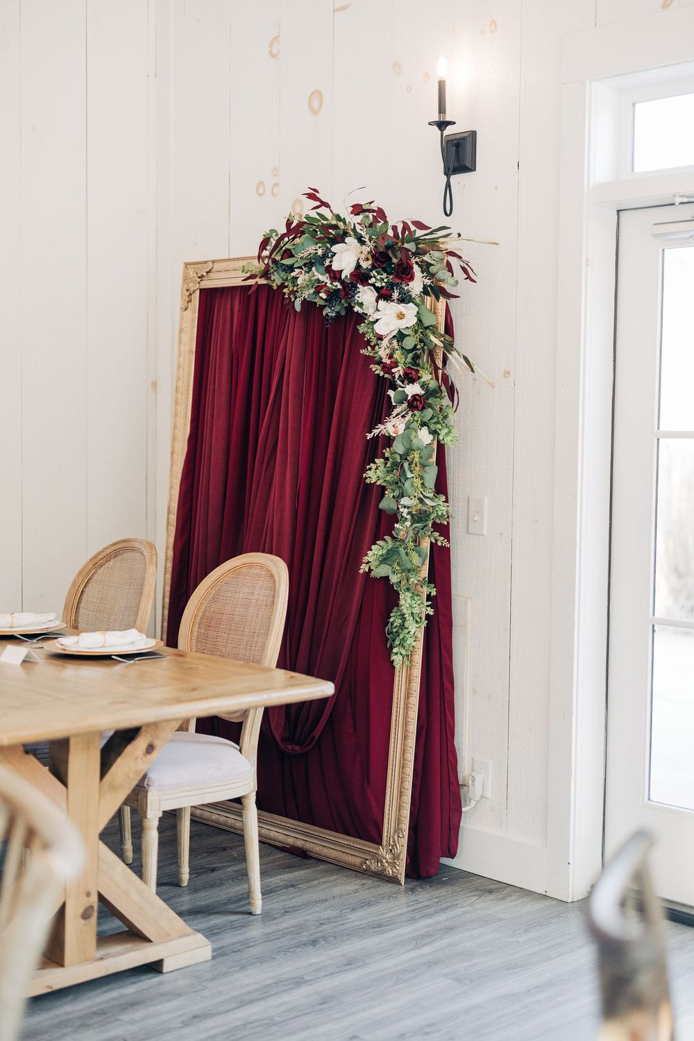 Modern event space with burgundy curtains, rattan chairs, and floral decorations against white walls.