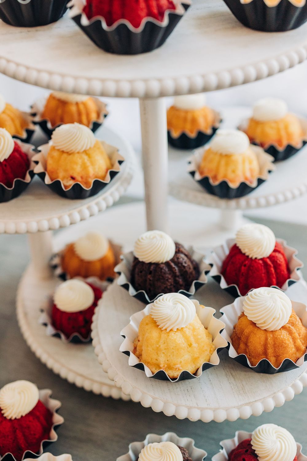 Colorful mini bundt cakes displayed on white scalloped serving platters.