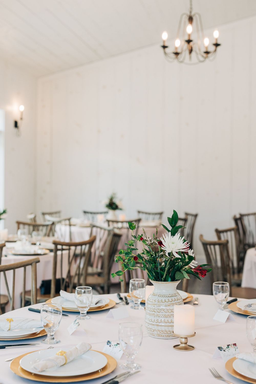 White reception hall with round tables set for a wedding featuring elegant place settings and greenery centerpieces.