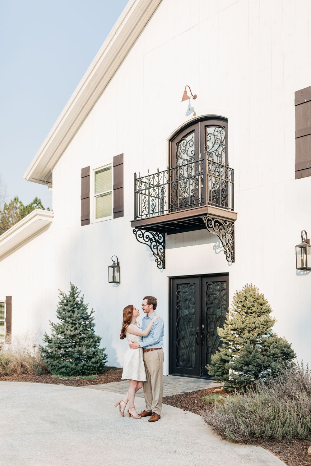 A romantic outdoor engagement photo sequence showing a couple posing near a white building with evergreen shrubs.
