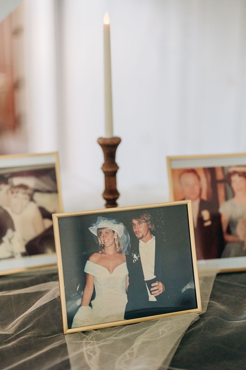 A wedding photo displayed on a table with a lit white candle in a wooden candlestick holder.