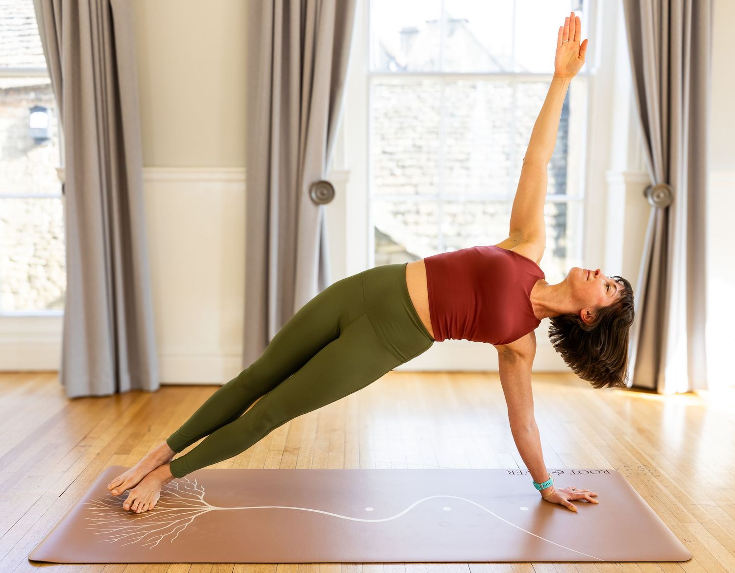 A person performs a challenging yoga pose on a mat in a bright studio with large windows.