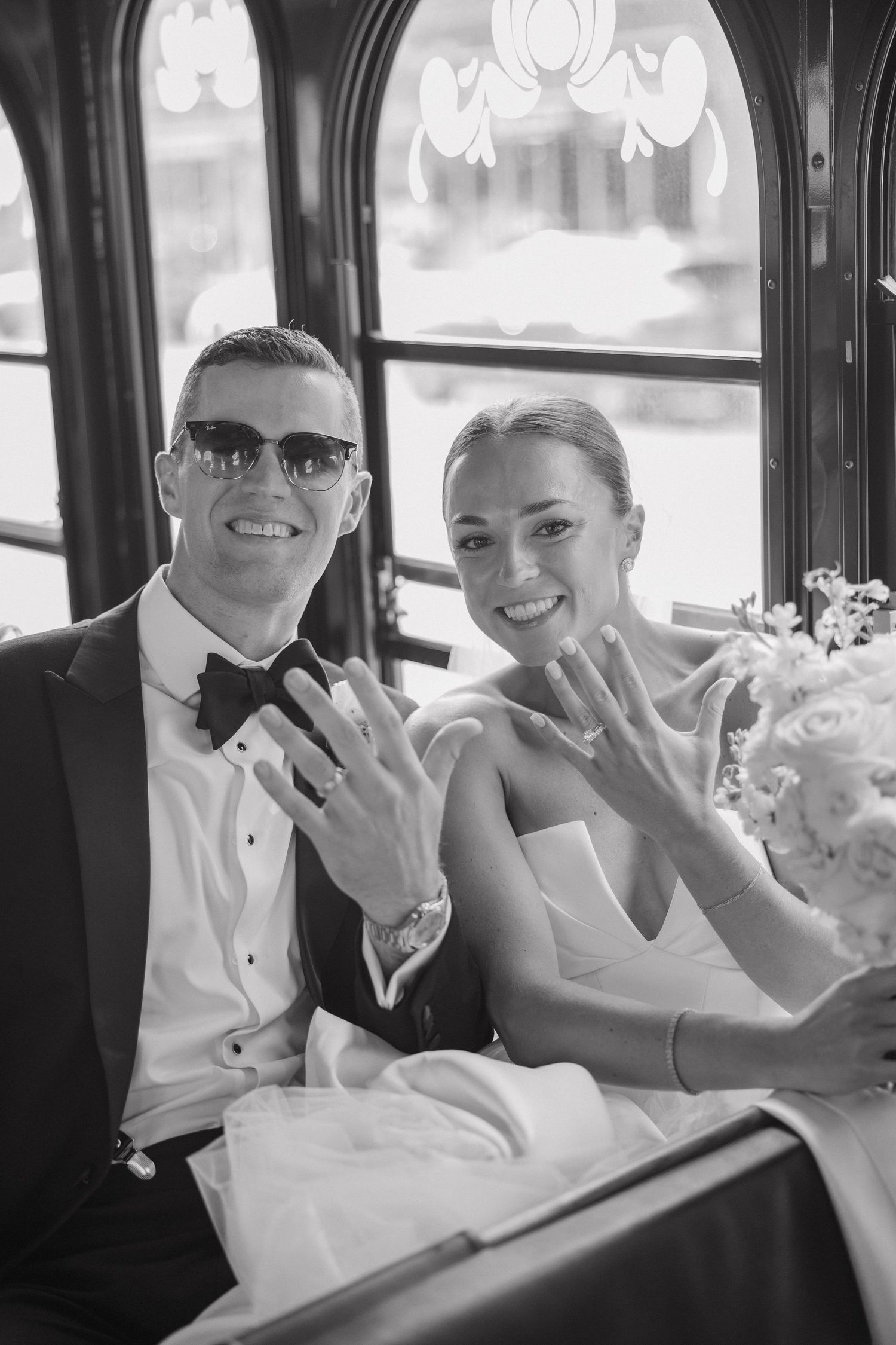 Wedding party smiles and waves while seated inside a classic trolley or bus.