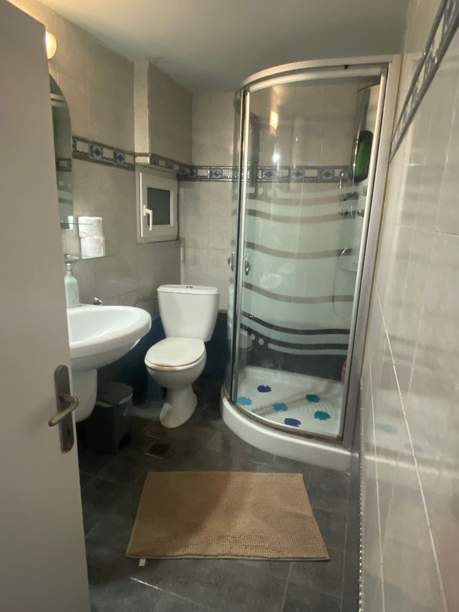 Modern bathroom interior with glass shower enclosure, wall-mounted toilet, and wood-look flooring in neutral tones.