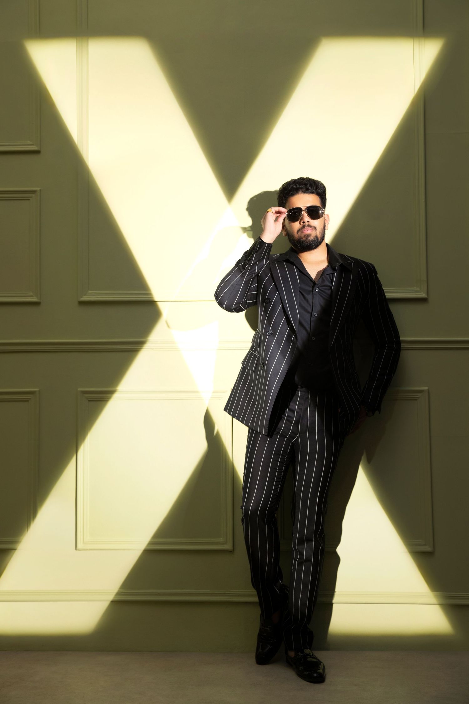 A figure in a black striped shirt poses dramatically against a wall with dramatic X-shaped lighting patterns.