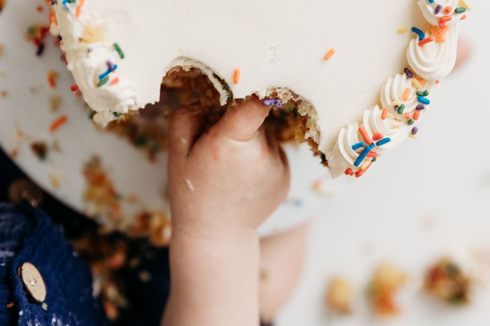 A close-up view of hands holding a vanilla cupcake with colorful sprinkles against a white background.