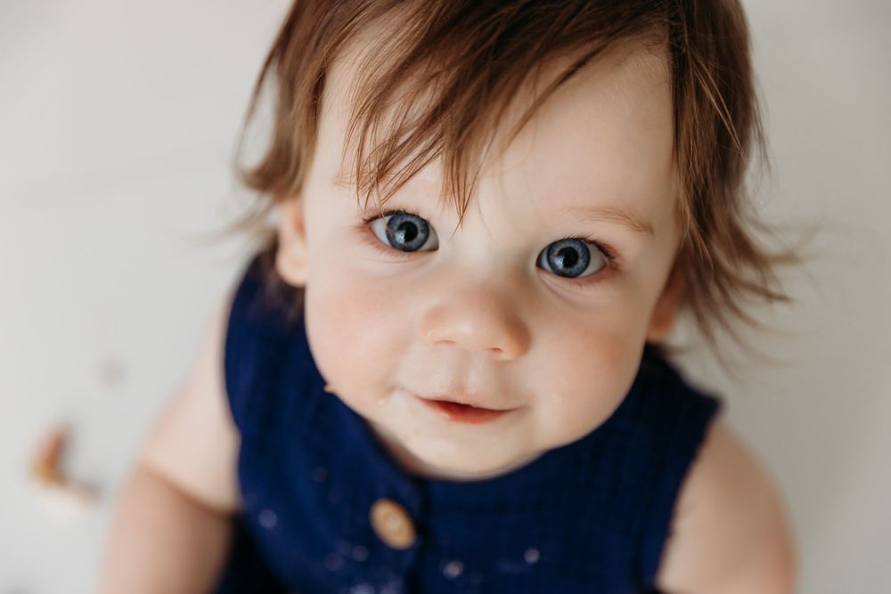 Close up view of baby in navy outfit with bright blue eyes against light background.
