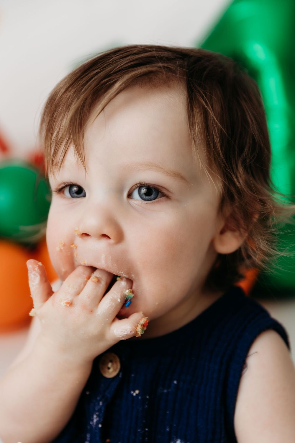 Series of photos showing baby eating cake with hands against green balloon backdrop.