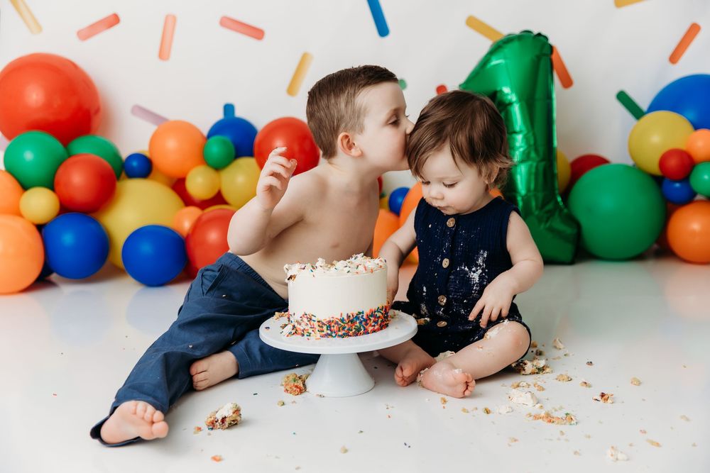 Baby in navy outfit enjoying first birthday cake smash photo session with balloons and decorations.