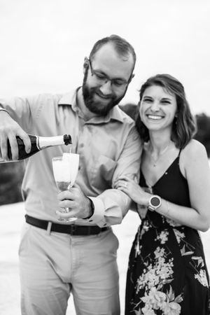 A couple shares a romantic moment while holding wine glasses and laughing together in a casual outdoor setting.